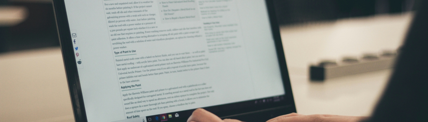 A laptop being typed on by a person, only their hands and forearms visible.